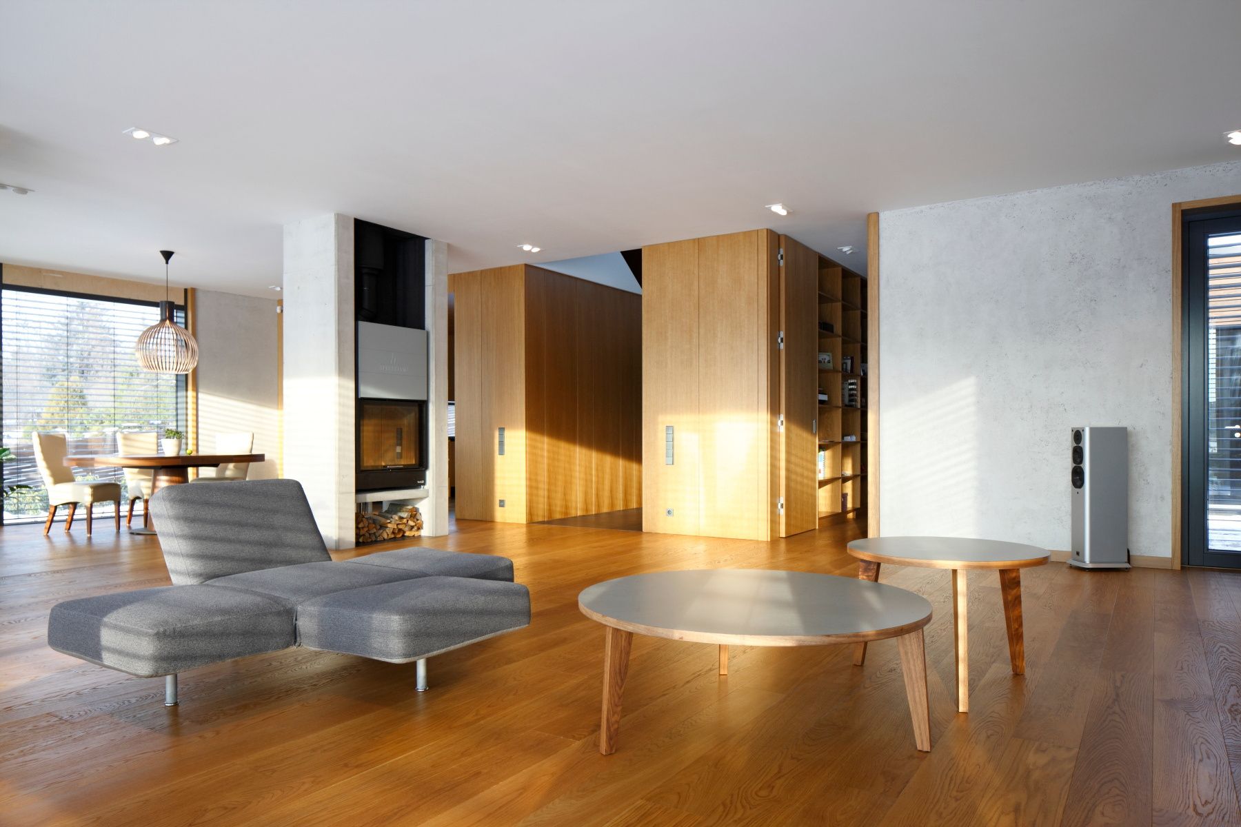 Open living space with oak-clad volumes, a grey lounger and a round table